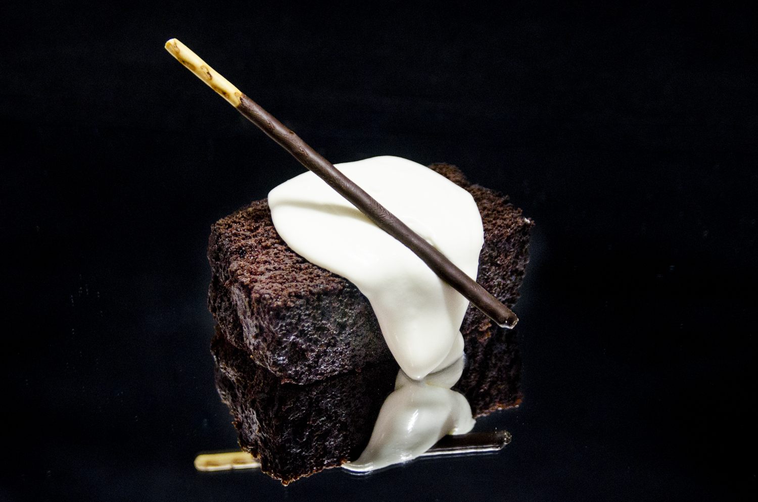 Postre de bizcocho de chocolate con nata montada y un lápiz de chocolate, sobre fondo oscuro
