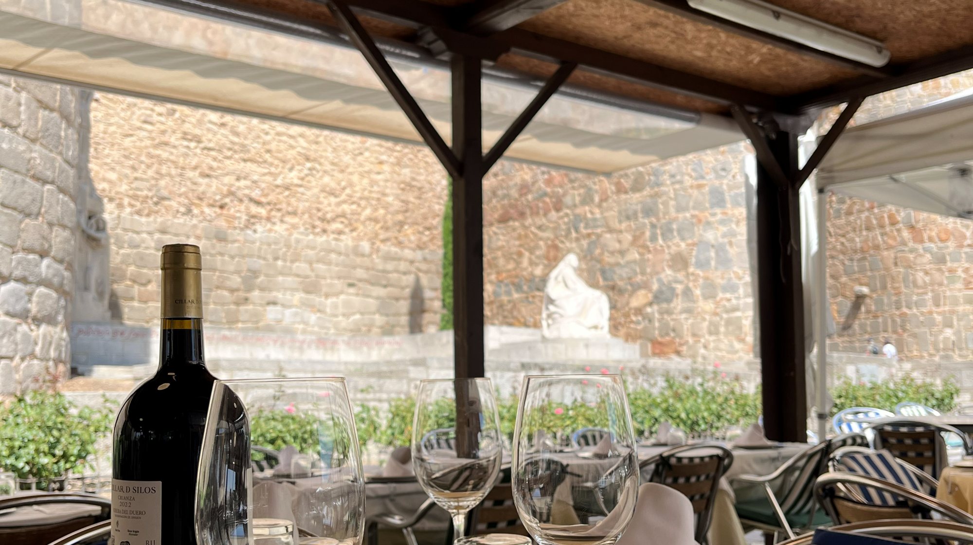 Mesa de la terraza de La Santa, con vino y copas, frente a la muralla de Ávila y el monumento a Santa Teresa