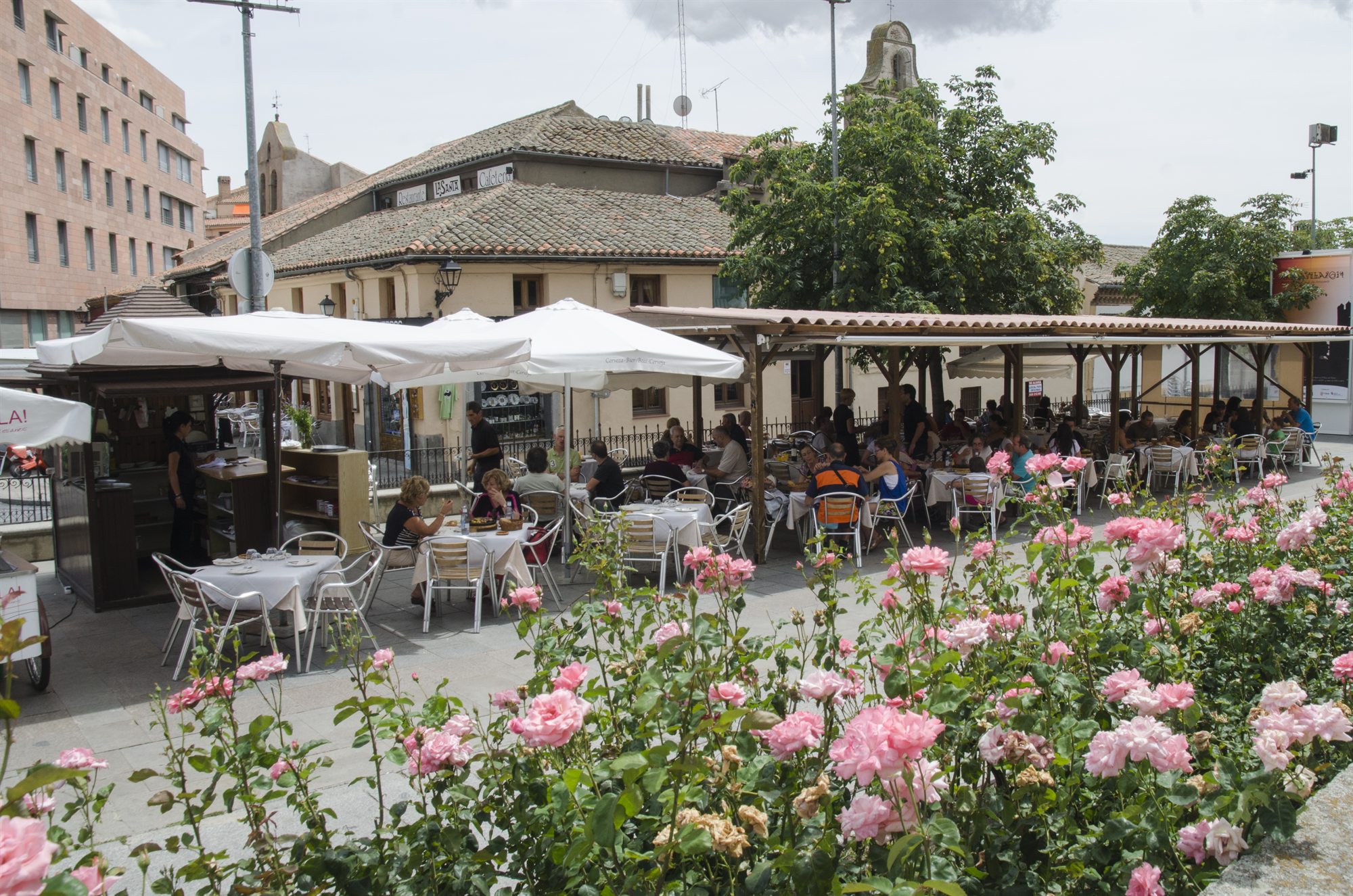 Terraza del Restaurante La Santa en la plaza de Ávila, con mesas, sombrillas y rosales en flor